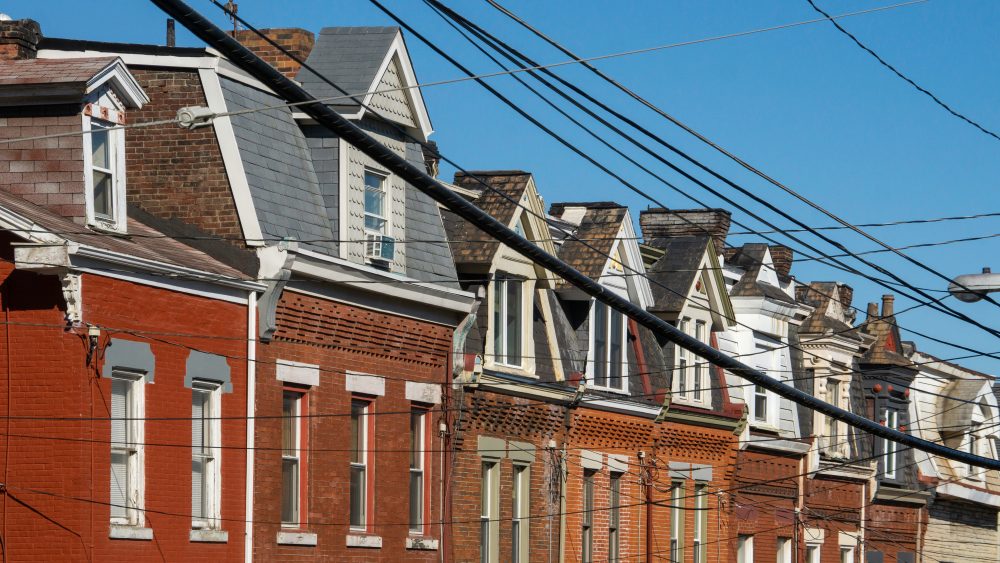 Row of old brick houses with gabled roofs and overhead power lines against a clear blue sky, much like neighborhoods where a Pittsburgh Chapter 7 Bankruptcy Attorney offers trusted legal guidance.